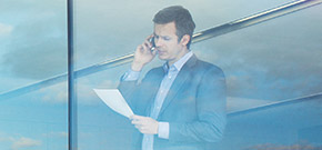 Mann im Anzug steht telefonierend am Fenster eines Bürogebäudes