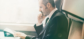 ein Mann im Businessoutfit sitzt in einem Zug und arbeitet auf seinem Tablet